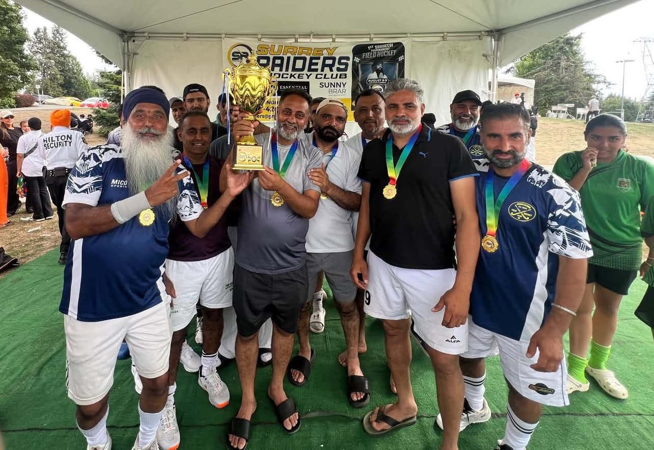 The Abbotsford Field Hockey Club squad gathered under the Surrey Raiders tent, holding the gold trophy up together with medals around their necks